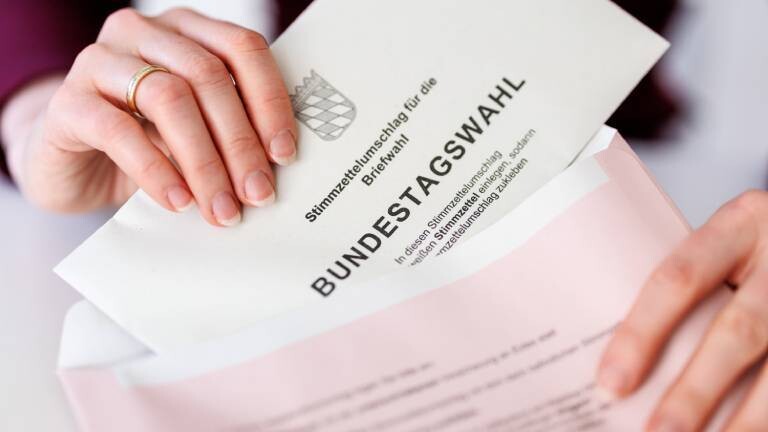 Eine Frau steckt in München (Bayern) einen Stimmzettelumschlag für die Briefwahl zur Bundestagswahl 2025 in den roten Wahlbriefumschlag.