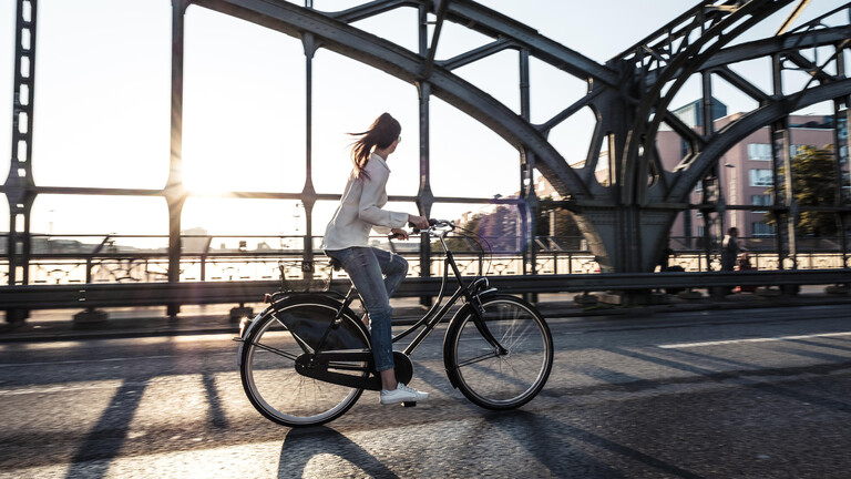 Fahrradfahrerin fährt im Sonnenschein über eine Stahlbrücke