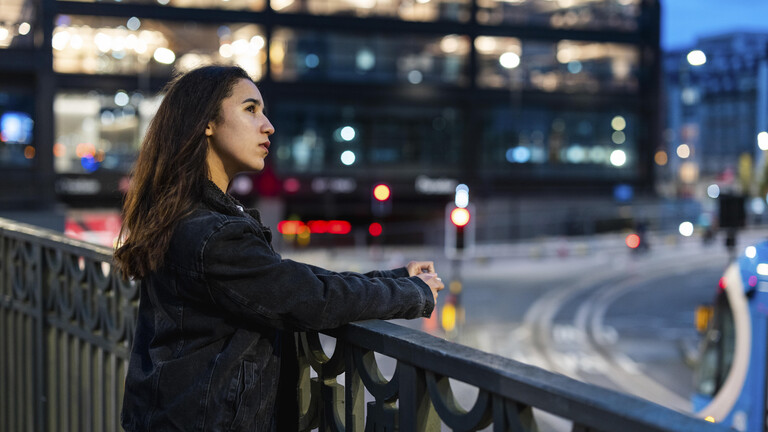 Eine Frau blickt in einer Stadt an einer breiten Kreuzung von einer Brücke in die Ferne.