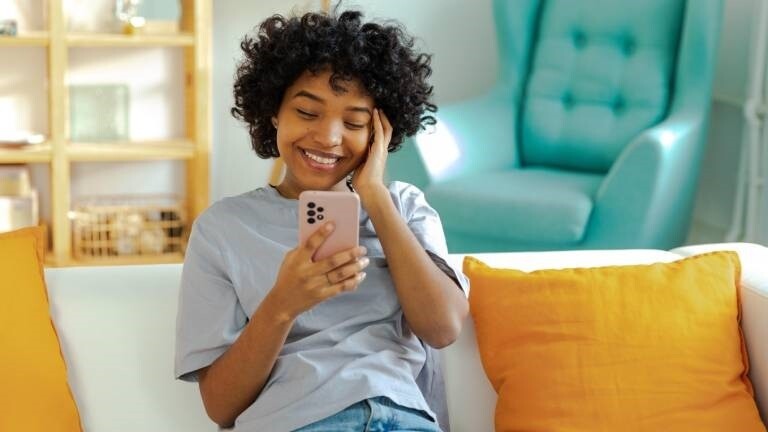 Eine junge Frau hält lächelnd ein Smartphone in der Hand