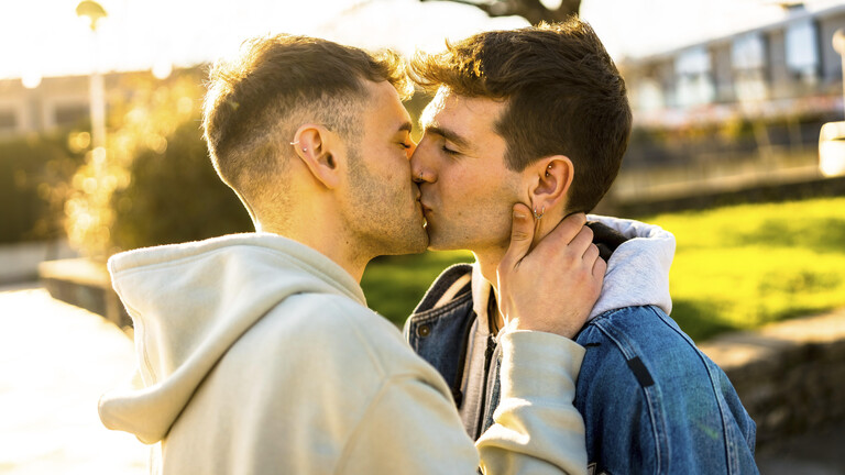 Zwei männlich gelesene Personen küssen sich auf den Mund.