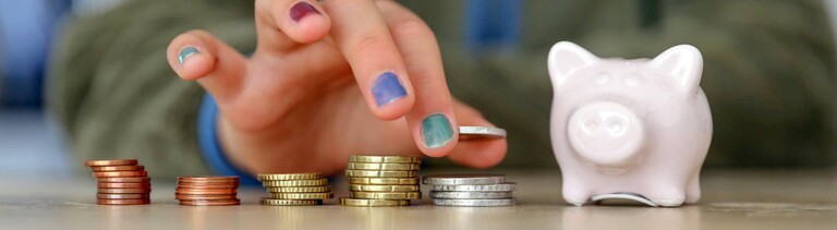 Hand mit lackierten Fingernägeln stapelt Geldmünzen neben einem Sparschwein