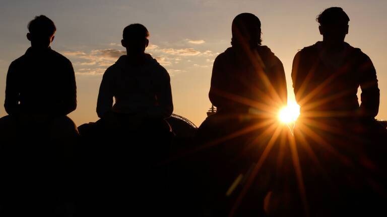 Silhouetten von Menschen, die nebeneinander auf einer Mauer sitzen