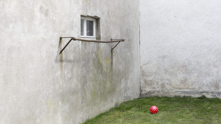 In einem etwas verfallenen Hinterhof in Deutschland liegt ein roter Ball auf dem Rasen.