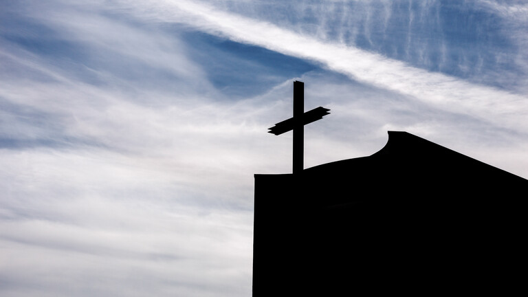 Ein Kreuz auf einer Kirche im Gegenlicht