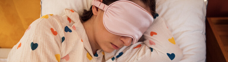 Eine Frau liegt mit einer Schlafmaske im Bett