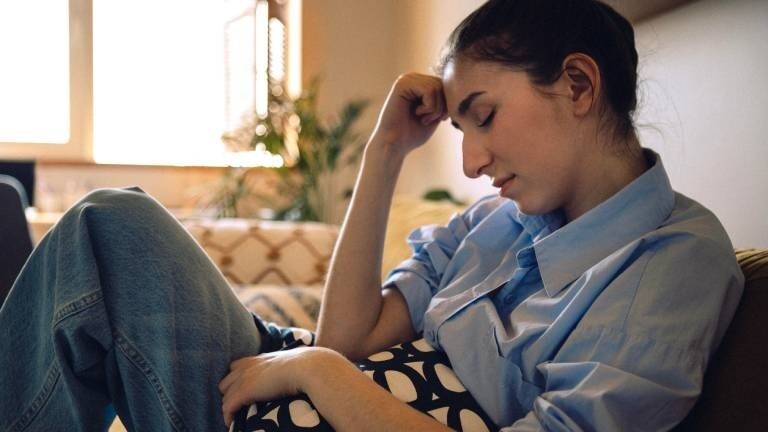 Eine Frau sitzt mit geschlossenen Augen auf dem Sofa und stützt ihren Kopf auf ihre Hand