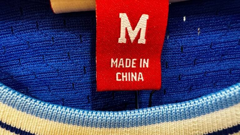 In der Nahaufnahme ist ein rotes Etikett mit der weißen Aufschrift „Made in China“ und der Größe M in einem Halsausschnitt eines Strickpullis zu sehen.