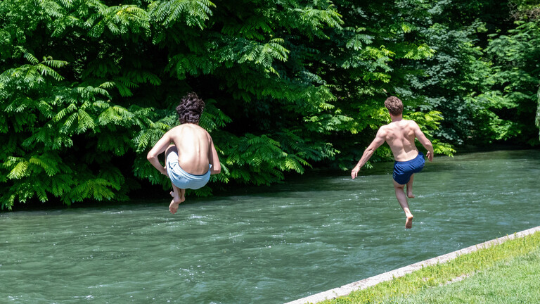 Zwei junge Männer springen zur Abkühlung in einen Bach