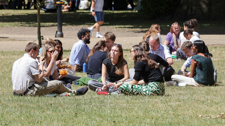 Junge Menschen sitzen in einer Gruppe im Sommer im Park.