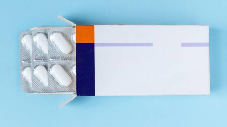 Geöffnete Schachtel mit weißen Tabletten in Blisterpackungen auf blauem Hintergrund