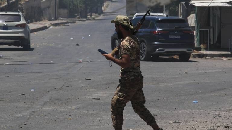 Ein Soldat der syrischen Sicherheitskräfte patrouilliert in den Straßen von Suweida und trägt ein Maschinengewehr während er auf sein Handy blickt.