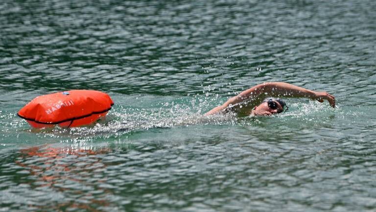 Ein Mann schwimmt im See. Er zieht eine Boje hinter sich her.