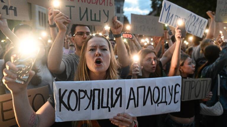 Kiewer Bürger nehmen an einer Kundgebung gegen die Umsetzung des Gesetzentwurfs Nr. 12414 teil, der die Arbeit der Sonderstaatsanwaltschaft zur Korruptionsbekämpfung und des Nationalen Antikorruptionsbüros in Kiew am 22. Juli 2025 regelt. Die Demonstrierenden halten Plakate hoch und leuchten mit ihren Handys. Eine Frau im Vordergrund skandiert Parolen.