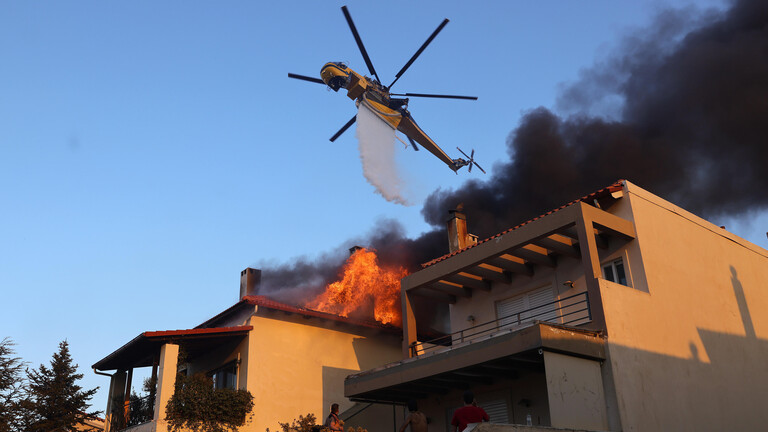Ein Lösch-Helikopter kippt Wasser über einem brennenden Haus aus