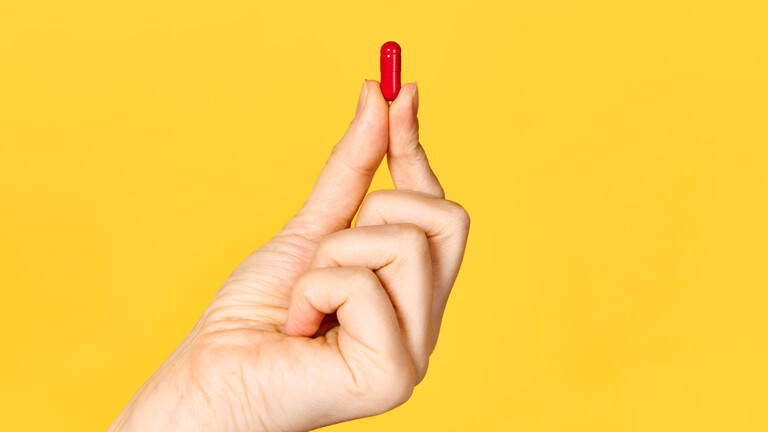 Eine Hand hält eine rote Kapsel zur Einnahme bei der Behandlung von Krankheiten