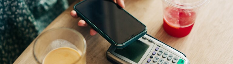 Nahaufnahme des kontaktlosen Bezahlens mit dem Mobiltelefon durch eine nicht erkennbare Person in einem Café.