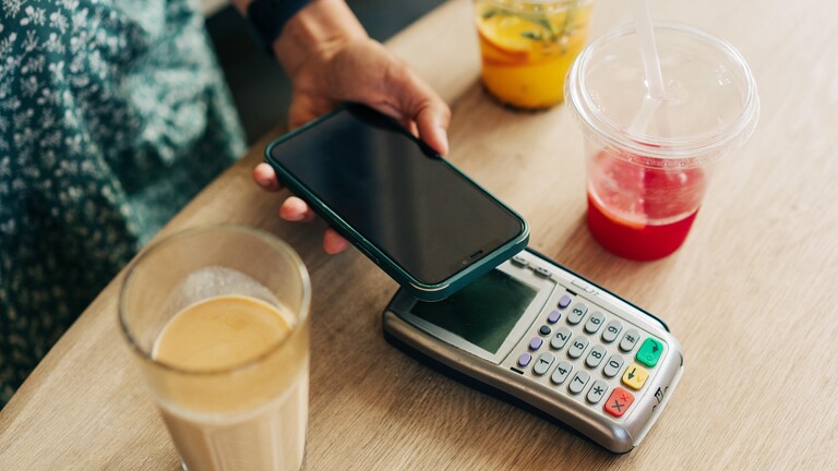 Nahaufnahme des kontaktlosen Bezahlens mit dem Mobiltelefon durch eine nicht erkennbare Person in einem Café.