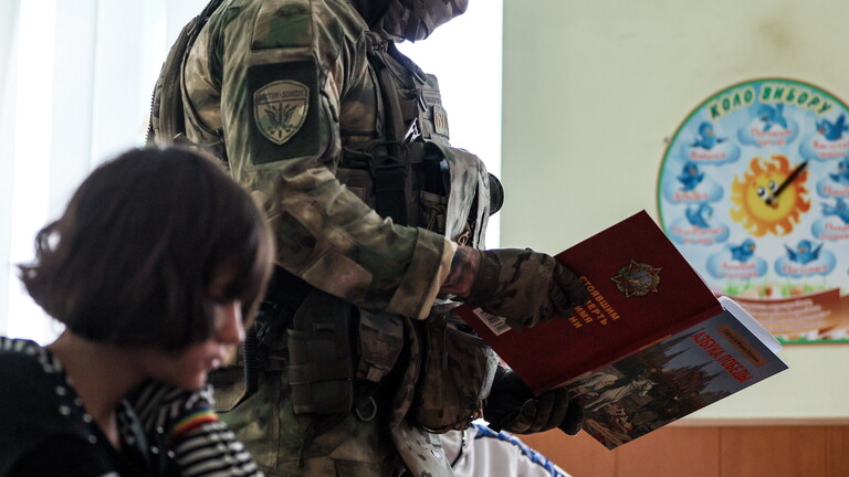 Ein Militär geht mit einem Buch an einem im Klassenraum sitzenden Schulkind vorbei (Kurakhovo, ukrainische und von Russland besetzte Region Donezk, 23.09.2025)
