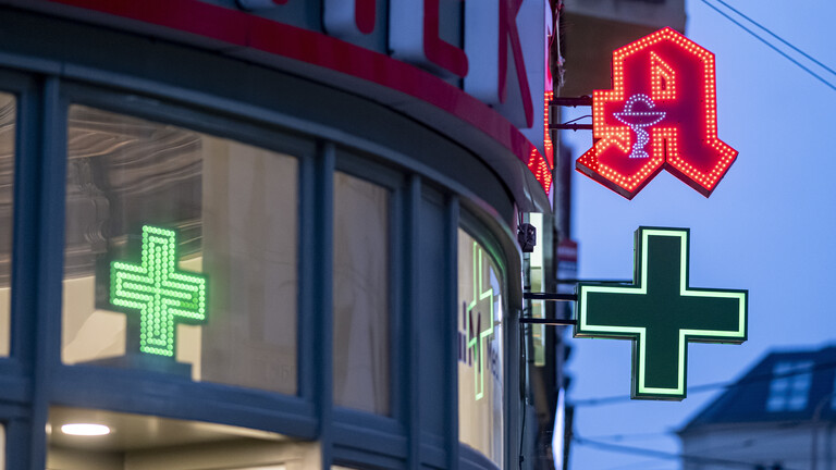 Das Apotheken-Logo leuchtet abends an einem Gebäude
