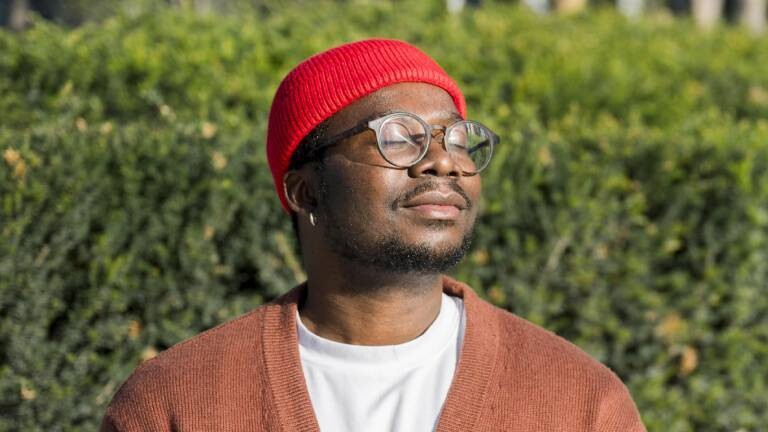 Mann mit roter Mütze und Strickjacke hält Gesicht in die Sonne