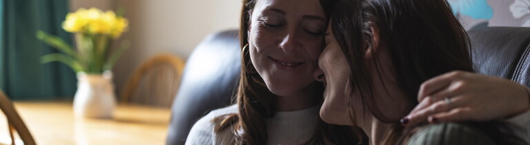 Zwei Freundinnen sitzen nebeneinander und umarmen sich