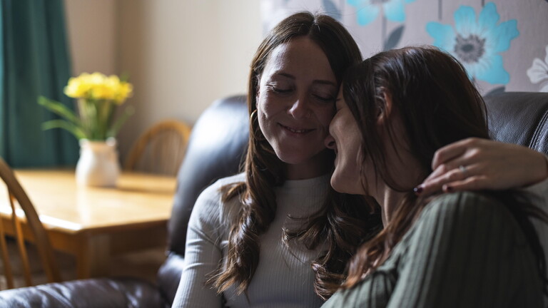 Zwei Freundinnen sitzen nebeneinander und umarmen sich