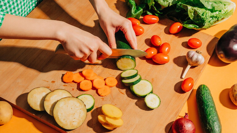 Eine Frau schneidet Gemüse klein auf einem großen Brett.