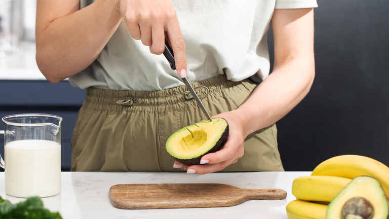 Frau schneidet Avocado mit einem Messer.