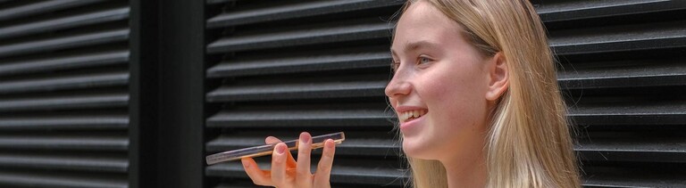 Frau steht vor schwarzen Rollläden und spricht ins Smartphone