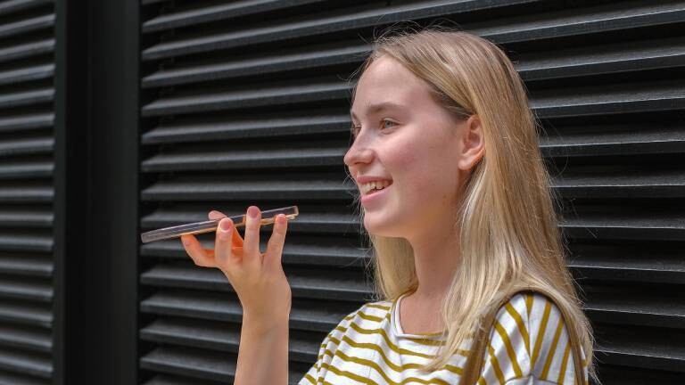 Frau steht vor schwarzen Rollläden und spricht ins Smartphone