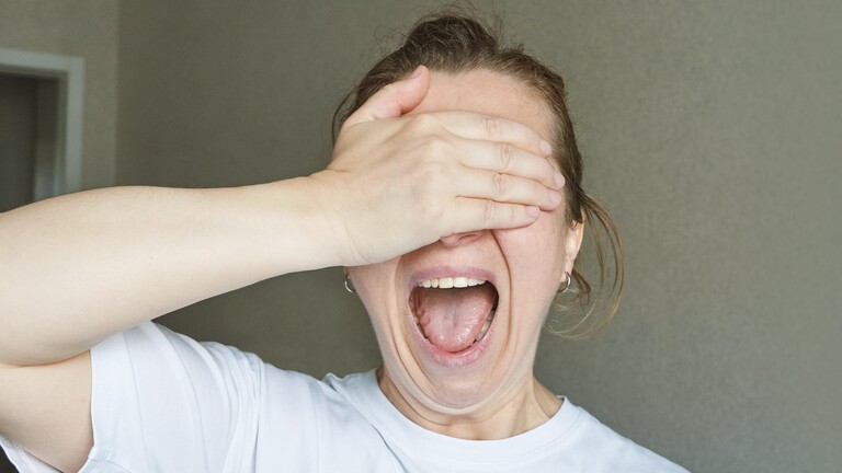 Eine Frau hält sich die rechte Hand vor den Kopf und öffnet den Mund