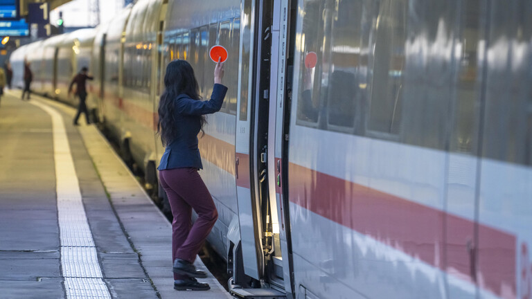 Mitarbeiterin der Deutsche Bahn steht an der Tür eines am Gleis stehenden ICEs und hält den Abfahrstab in die Höhe (Hauptbahnhof Essen, 11.11.2025)
