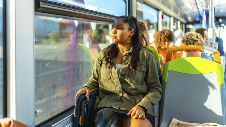 Eine junge Frau sitzt am Fenster eines öffentlichen Verkehrsbusses und schaut nachdenklich nach draußen