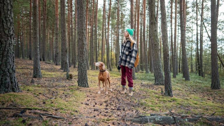 Eine Frau steht mit einem Hund im Wald