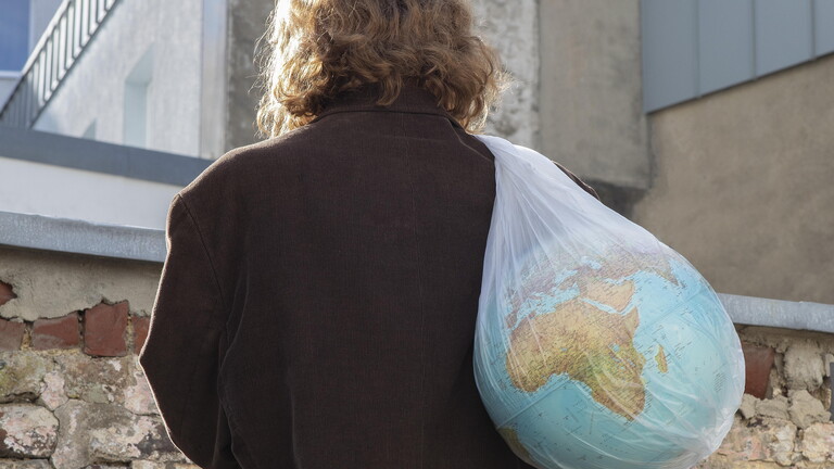 Frau trägt einen Globus in einer Plastiktüte in Richtung eines Mülleimers