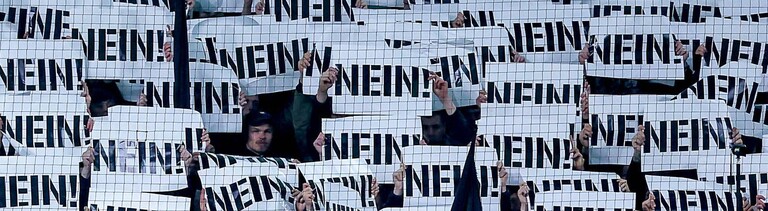 Fußballfans halten Schilder als Protest gegen die Pläne des Bundesinnenministers mit der Aufschrift „NEIN“ vor ihre Gesichter (Borussia-Park Mönchengladbach, 28.11.2025)