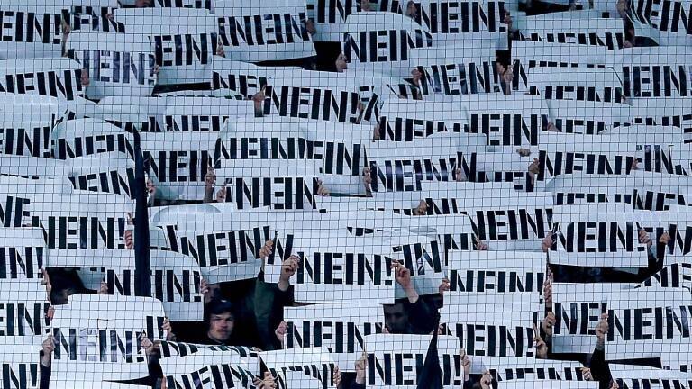 Fußballfans halten Schilder als Protest gegen die Pläne des Bundesinnenministers mit der Aufschrift „NEIN“ vor ihre Gesichter (Borussia-Park Mönchengladbach, 28.11.2025)