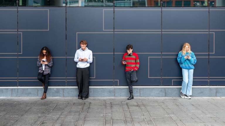 Mehrere junge Menschen stehen an einer Wand und haben Smartphones in der Hand