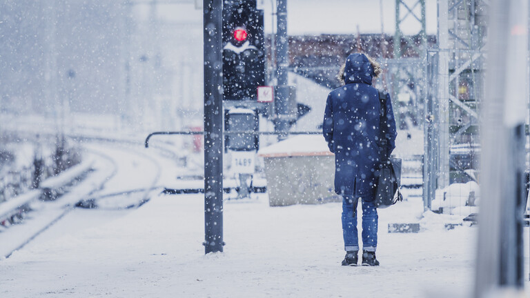 Ein Mann steht an einem leeren schneebedeckten Bahnsteig.