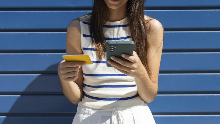 Eine Frau hält Kreditkarte und Smartphone in der Hand.