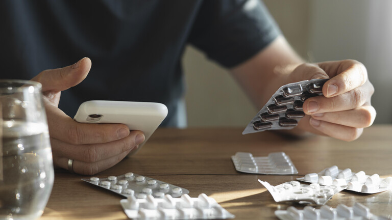 Jemand hält in einer Hand ein Smartphone, in der anderen einen Blister mit Tabletten