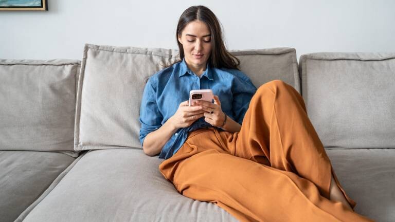 Frau sitzt in Arbeitskleidung auf dem Sofa und textet auf dem Smartphone mit Bekannten.