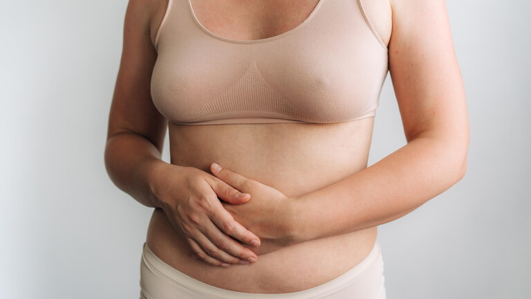Eine Frau in beiger Unterwäsche hält sich ihre Hände auf den Bauch. Im Bild ist nur ihr Körper nicht ihr Gesicht.