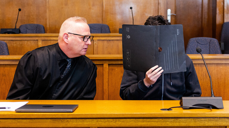 Ein Verteidiger sitzt neben seinem Mandanten in einem Saal des Landgerichts Saarbrücken. Der Angeklagte hat einen Polizisten mit einer Dienstwaffe erschossen.