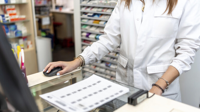Eine Apothekerin steht in ihrem weißen Laborkittel hinter der Kasse.