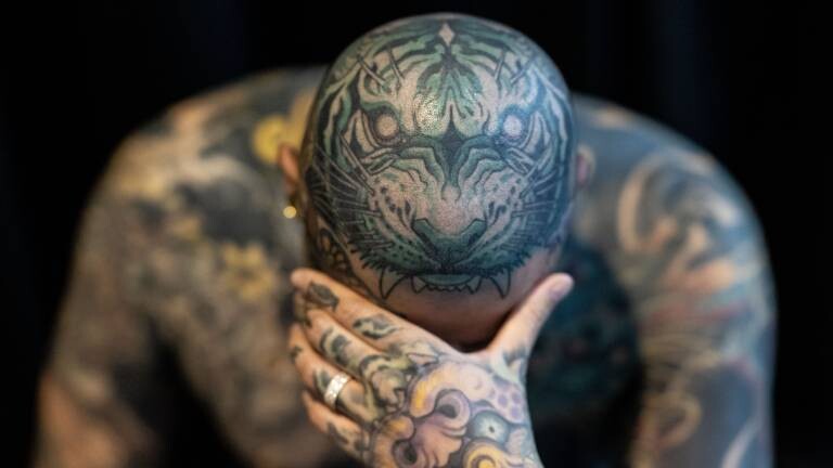 Ein Mann zeigt seine Tattoos, wobei der Kopf mit dem Bild eines Tigers verziert ist
