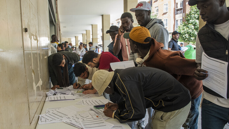 Migranten stehen Schlange und füllen Formulare aus