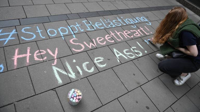 Eine Frau schreibt ihre Erfahrungen mit Catcalling mit Kreide auf den Boden