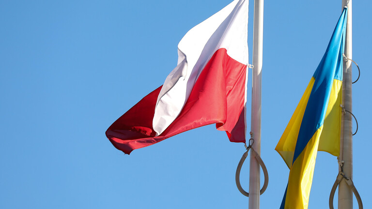 Die Flagge Polens und die der Ukraine hängen nebeneinander an einem Mast. Der Himmel ist blau und wolkenlos.
